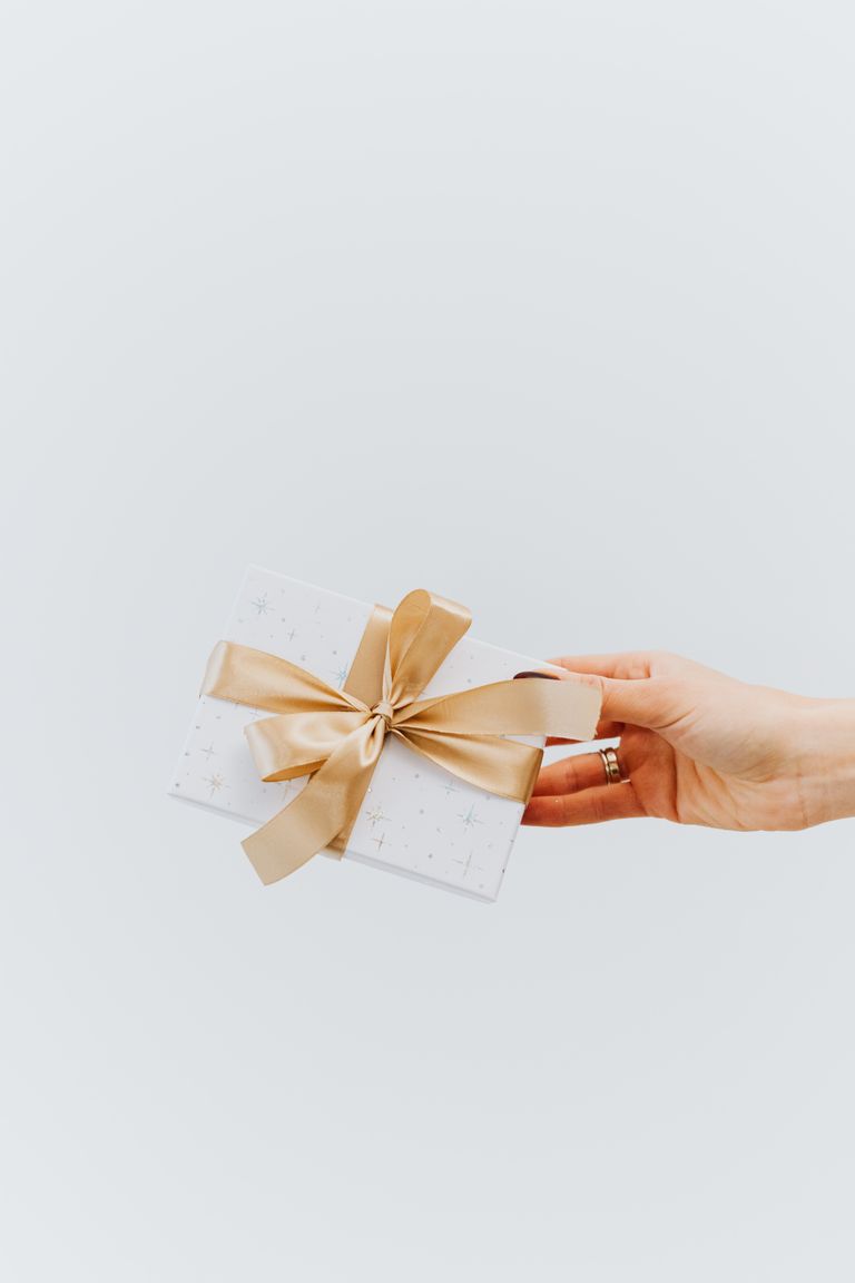 A hand holding an elegantly wrapped gift box with a gold ribbon on a white background.